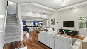 Sala de estar moderna com um sofá cinzento, uma televisão de tela plana e uma escada que leva a uma área de cozinha.