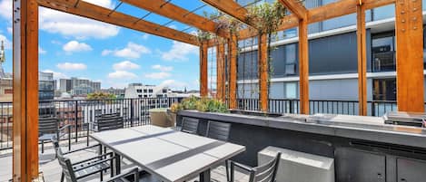 Eine Terrasse im Freien mit Tisch und Stühlen, einer Holz-Pergola und Blick auf eine Stadtlandschaft.