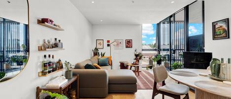 Una sala de estar moderna con un sofá, una mesa de comedor con sillas, un escritorio para computadora y un ventanal con vista a la ciudad.