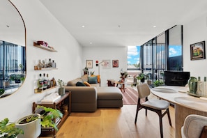 Un salon moderne comprenant un canapé, une table à manger avec des chaises, un bureau et une grande fenêtre donnant sur la ville.