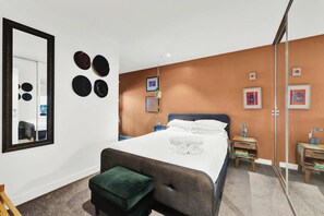 A bedroom with a bed, a green ottoman, a mirror, and wall decorations. - Stylish Inner City Apartment (Collingwood)