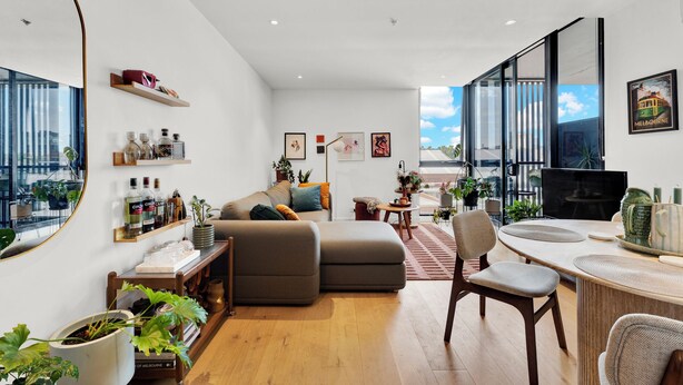 A modern living room with a sofa, a dining table with chairs, a computer desk, and a large window with a city view. - Stylish Inner City Apartment (Collingwood)