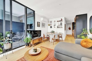 A modern living room with a sofa, dining table, chairs, and a TV. - Stylish Inner City Apartment (Collingwood)
