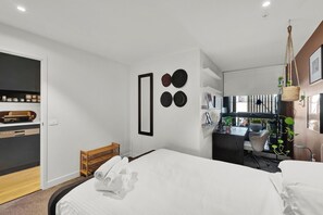 A modern hotel room with a bed, a desk, and a view of the city. - Stylish Inner City Apartment (Collingwood)