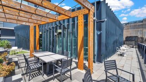 An outdoor patio with a table and chairs, a wooden pergola, and a modern building with large windows. - Stylish Inner City Apartment (Collingwood)