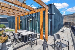 An outdoor patio with a table and chairs, a wooden pergola, and a modern building with large windows.