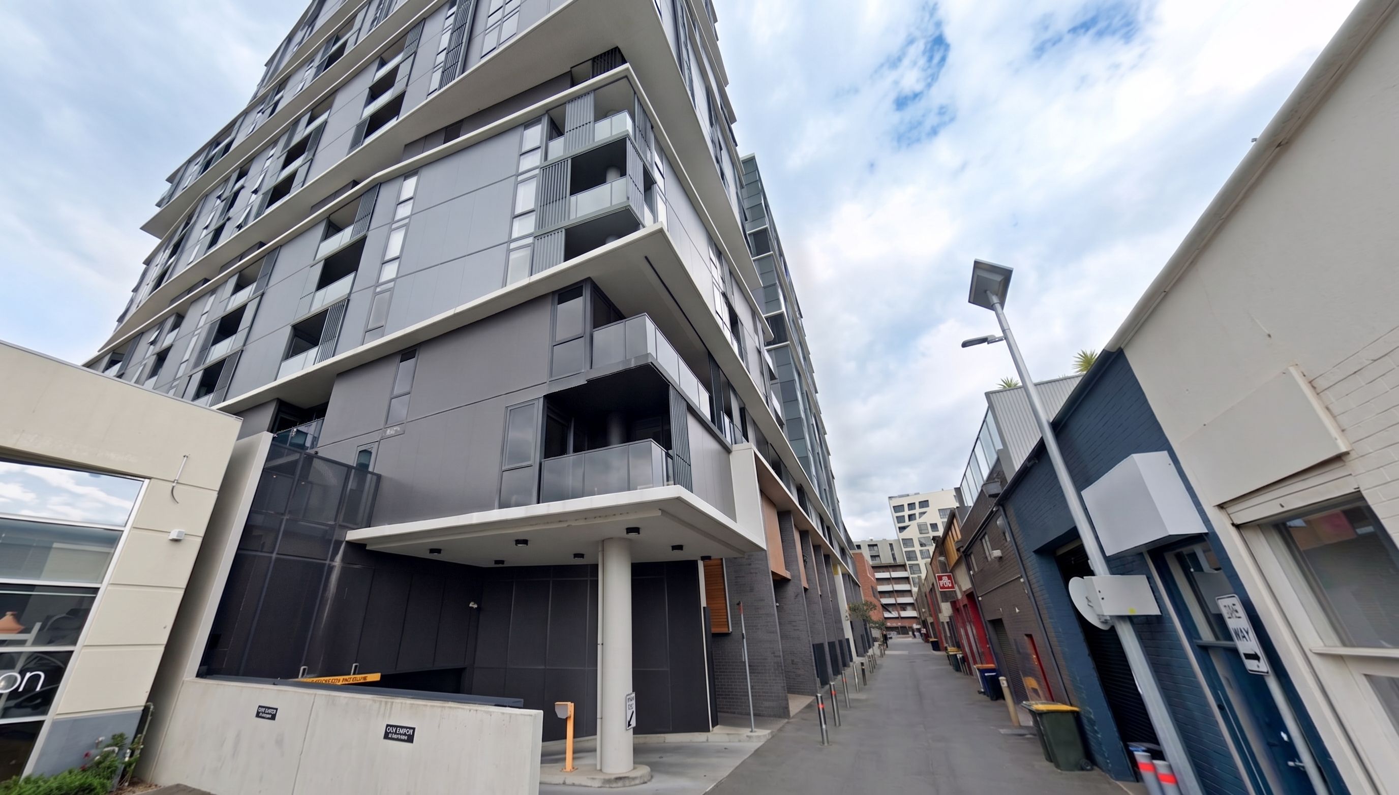 A multi-story residential building with balconies, a covered entrance, and a narrow street.
