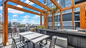 An outdoor terrace with a table and chairs, a wooden pergola, and a view of a cityscape. - Stylish Inner City Apartment (Collingwood)