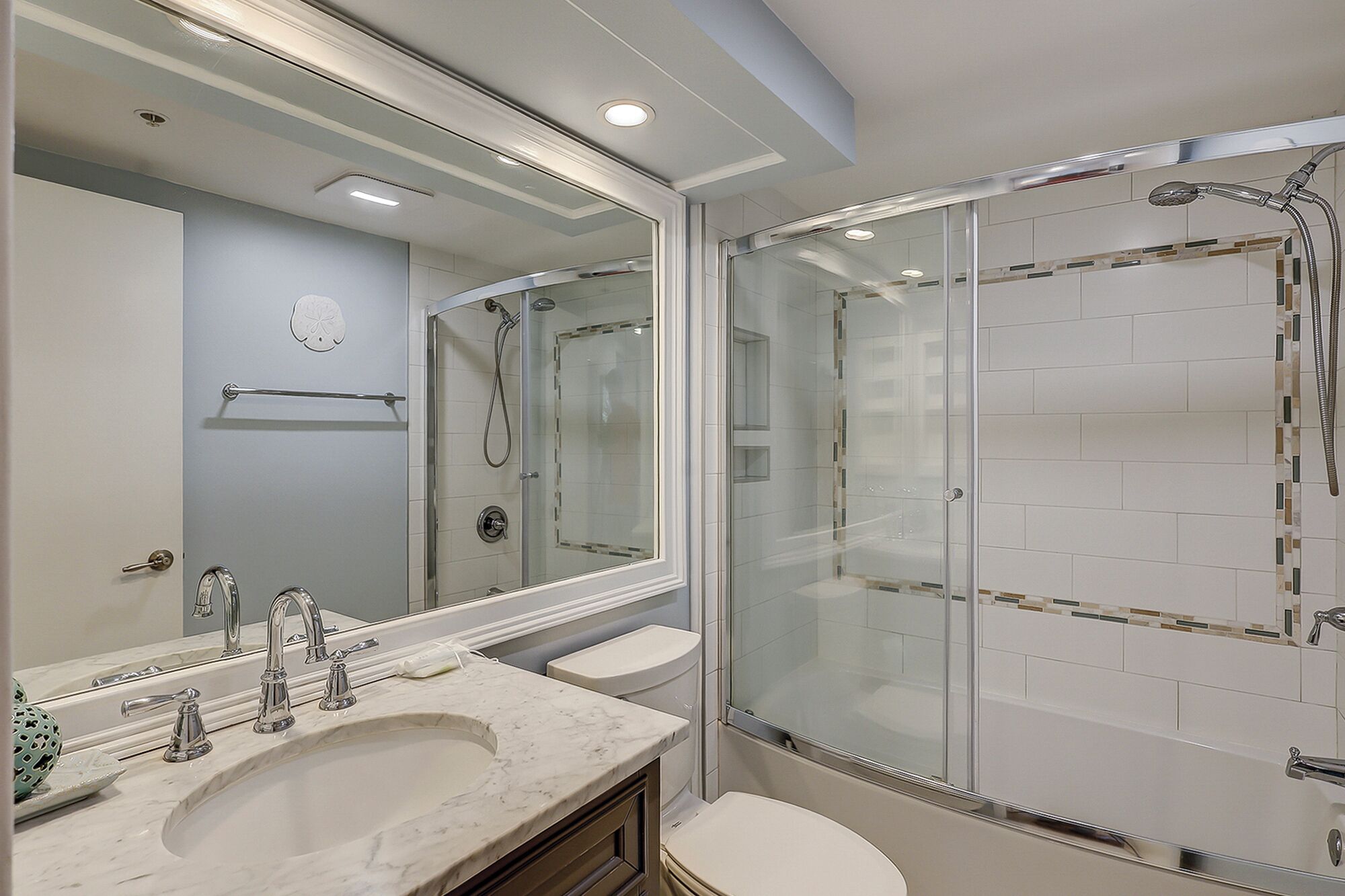 Een moderne badkamer met een glazen douchecabine, een grote spiegel en een marmeren wastafel.