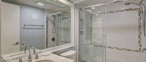 Een moderne badkamer met een glazen douchecabine, een grote spiegel en een marmeren wastafel.