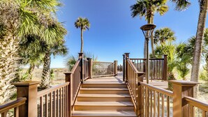 A wooden boardwalk with railings, leading towards palm trees and a clear blue sky. - Oceanfront beach villa in Palmetto Dunes (Hilton Head Island)