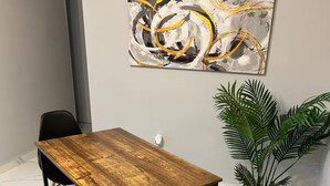 Un comedor con una mesa de madera y banco, sillas negras, una planta en maceta y un cuadro abstracto moderno en la pared.