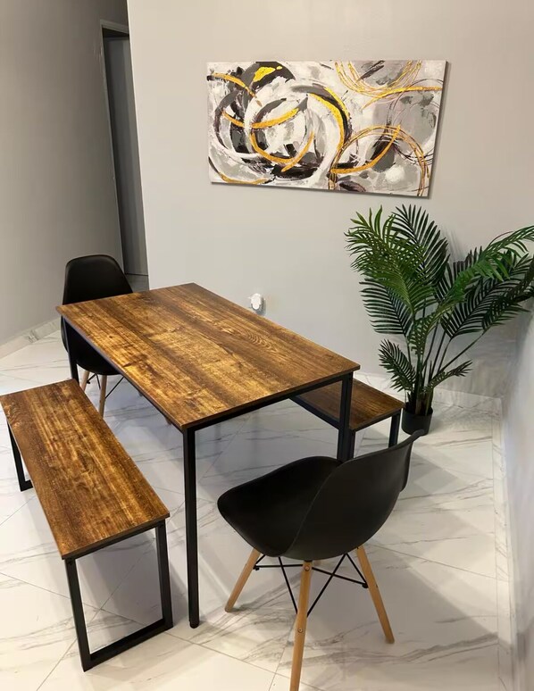 A dining area with a wooden table and bench, black chairs, a potted plant, and a modern abstract painting on the wall.