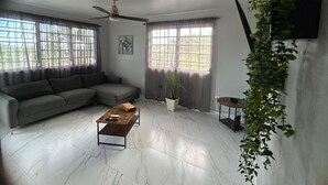 Una sala de estar con un sofá seccional, una mesa de centro, una planta en maceta y un ventilador de techo.