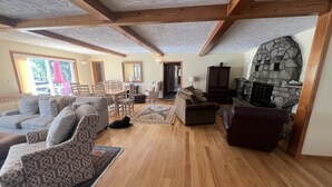 A spacious living room with wooden floors, a stone fireplace, and a dining area with wooden furniture. - On Wyman Pond. Home on sprawling property with a pond, hiking & wildlife. (Sidney Center)