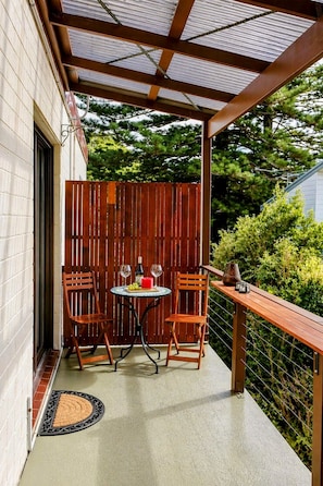 A covered outdoor patio with a table and two chairs, a wooden fence, and a doormat. - Anam by the Sea – Private Coastal Escape in the Royal National Park (Bundeena)