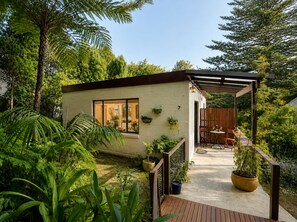 Een modern huis met een overdekte patio, omgeven door weelderige begroeiing en diverse planten.