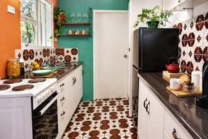 A kitchen with a stove, sink, and cabinets, a refrigerator, and a window with plants. - Anam by the Sea – Private Coastal Escape in the Royal National Park (Bundeena)