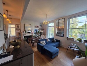 A spacious living room with a blue sofa, a dining area, and a kitchen visible through a large window.