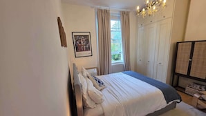 Ein Schlafzimmer mit einem Bett, einem Nachttisch, einer Lampe, einem Fenster mit Vorhängen, einer Chandelier und einem Kleiderschrank.