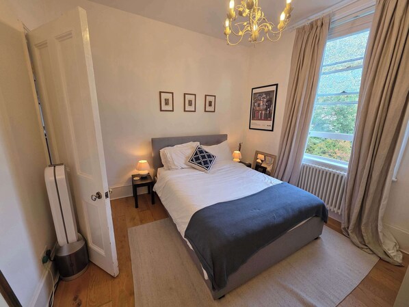 A neatly arranged bedroom with a bed, bedside lamps, a radiator, and a window with curtains.