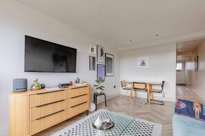 A modern living room with a flat-screen TV, wooden cabinet, and a dining area with a table and chairs. - Gorgeously Designed 2BD Flat, Heart of East London (Greater London)