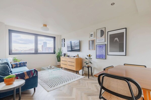A modern living room with a sofa, coffee table, TV, and dining table. - Gorgeously Designed 2BD Flat, Heart of East London (Greater London)