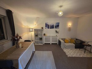 Un salon moderne comprenant un canapé, une table à manger, une console blanche et un luminaire suspendu au plafond.