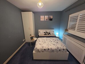 A bedroom with a bed, a wardrobe, a bedside table, and a radiator.