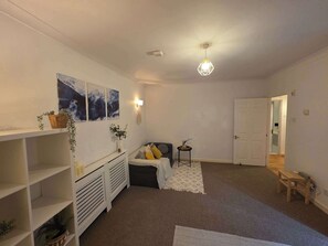 Une pièce comprenant un canapé, une petite table, une étagère fixée au mur avec des plantes et un luminaire au plafond.