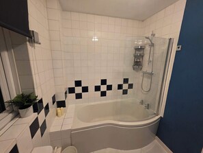 Une salle de bain avec une baignoire, une douche et un mur recouvert de carreaux disposés en motif à carreaux.