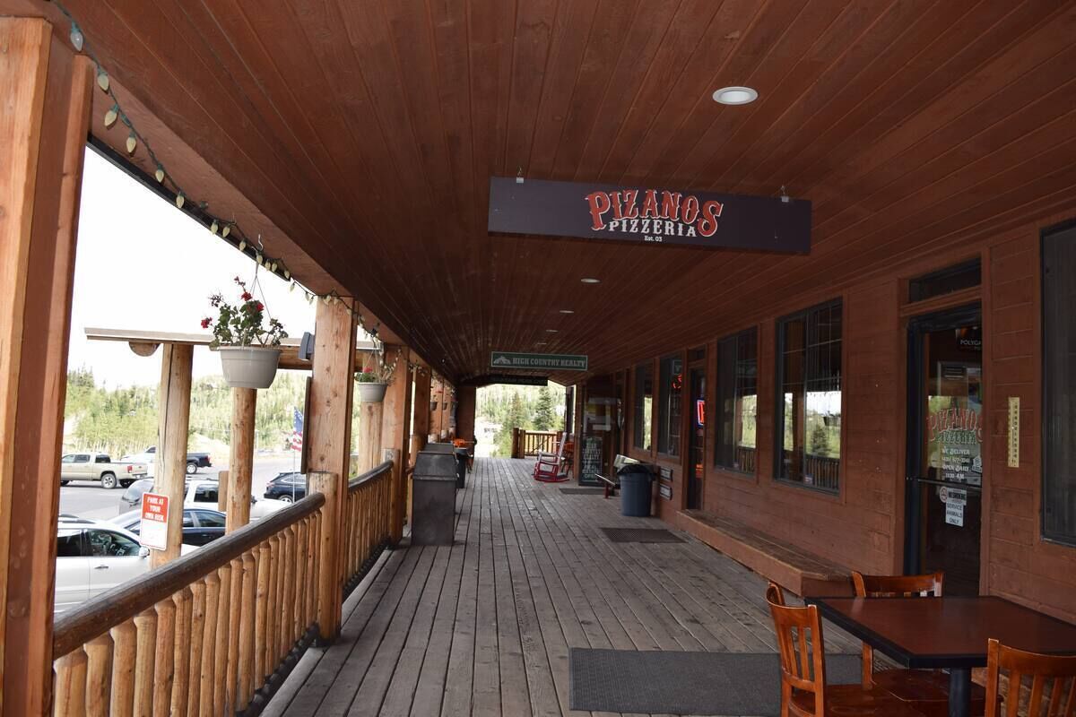 A wooden deck with a sign for 'PIZANOS PIZZERIA' and a view of parked cars.