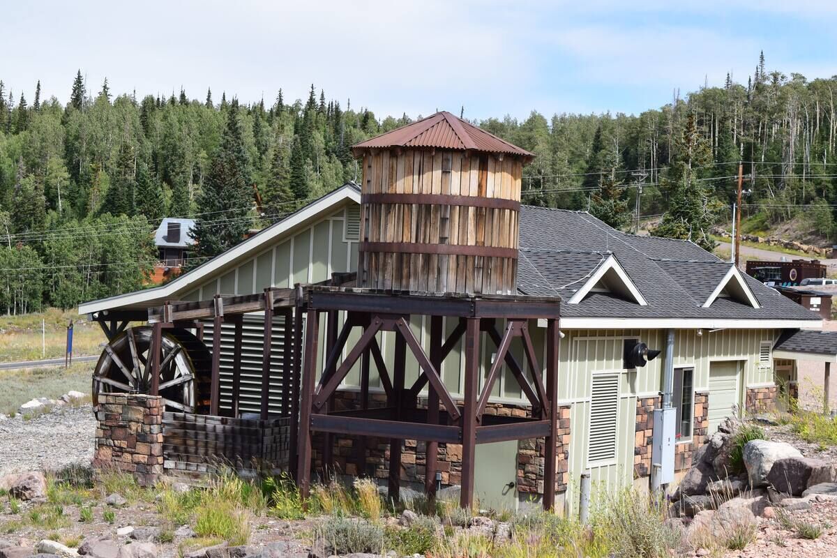 A rustic building with a large water wheel, a wooden tower, and a stone foundation.