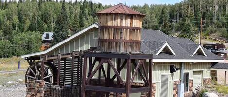 A rustic building with a large water wheel, a wooden tower, and a stone foundation.