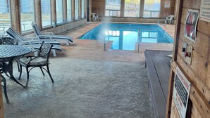A covered pool area with a wooden ceiling, a pool table, and lounge chairs.