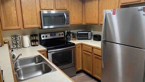 A kitchen with wooden cabinets, stainless steel appliances including a microwave, oven, and refrigerator, and a double sink.