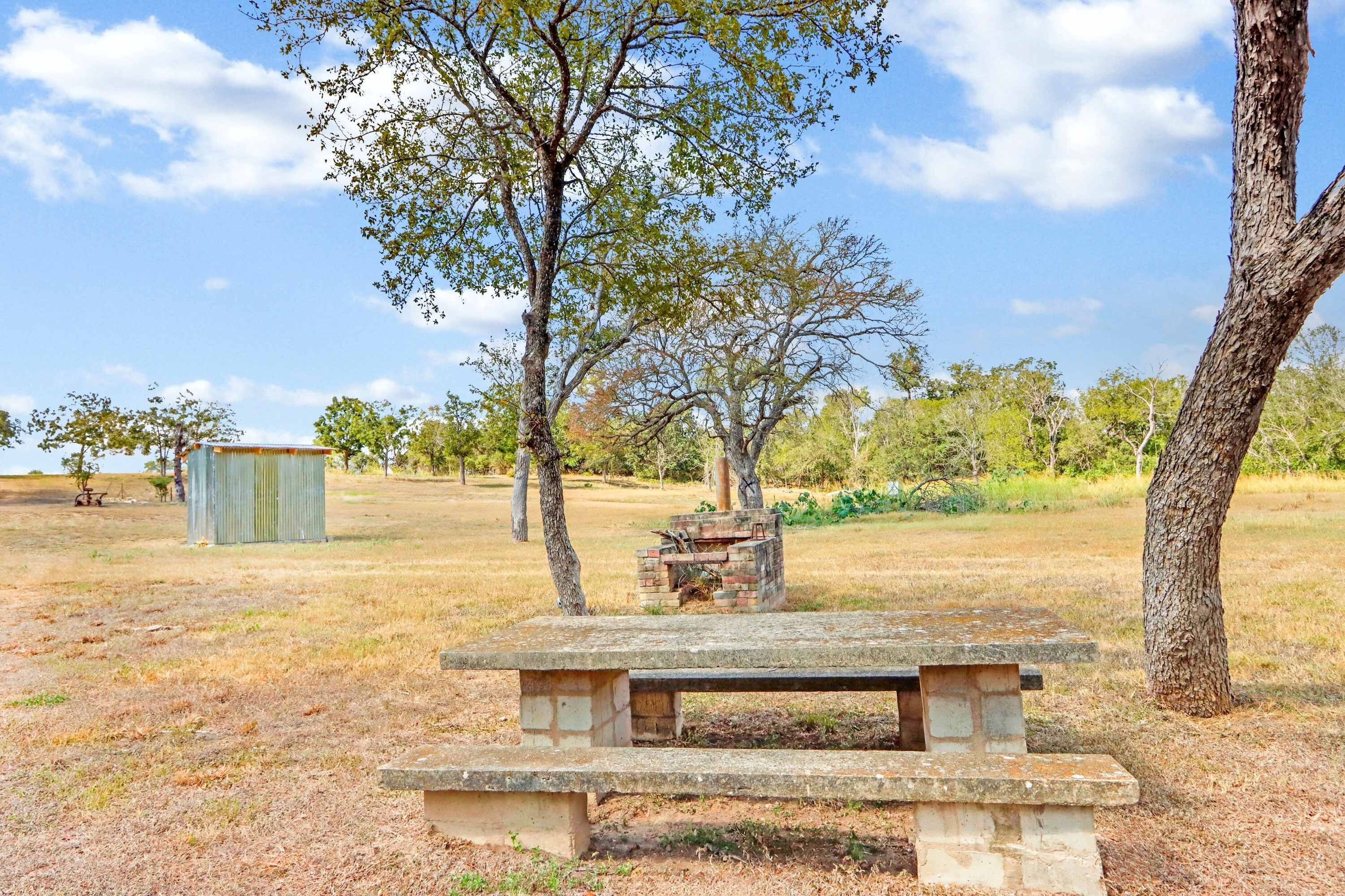 A picnic table in a park with trees and a small structure in the background.