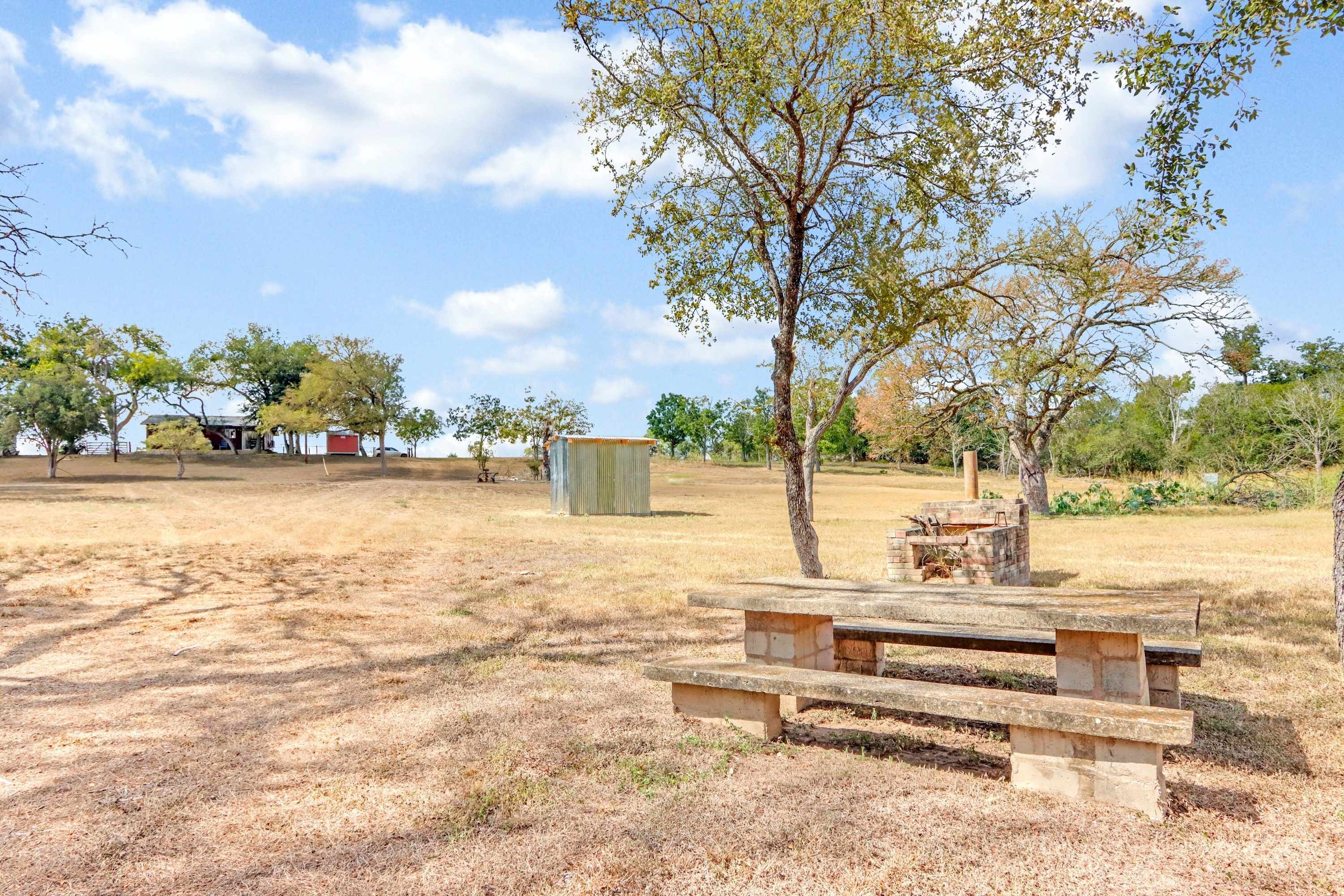 A picnic area with a wooden bench and a fire pit, surrounded by trees and open space.