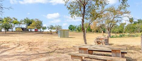 A picnic area with a wooden bench and a fire pit, surrounded by trees and open space.