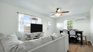 A living room with a sofa, a TV on a stand, a dining table with chairs, and a ceiling fan. - Guadalupe Bend Hideaway For 5 (New Braunfels)