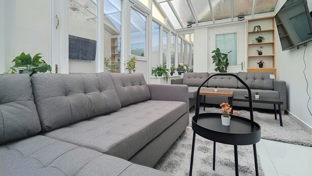 Ein modernes Wohnzimmer mit einem grauen Ecksofa, einem runden schwarzen Couchtisch und einem an der Wand montierten Fernseher.