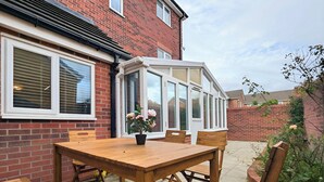 Eine Terrasse mit Holztisch und -stühlen, einem Blumentopf und einem Wintergarten.