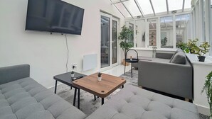 Ein modernes Wohnzimmer mit Flachbildfernseher, grauen Sofas, einem Holztisch und einer Glasdecke.