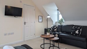 A modern living room with a black sofa, a small round table, a TV mounted on the wall, and a door. - This is a large three-story house, located near the city centre. A short 4-minute drive (1 mile) will take you to the city centre, Albert Dock, ACC. Convenient public transportation is available with a 10-minute bus ride from the city. centre. (Merseyside)