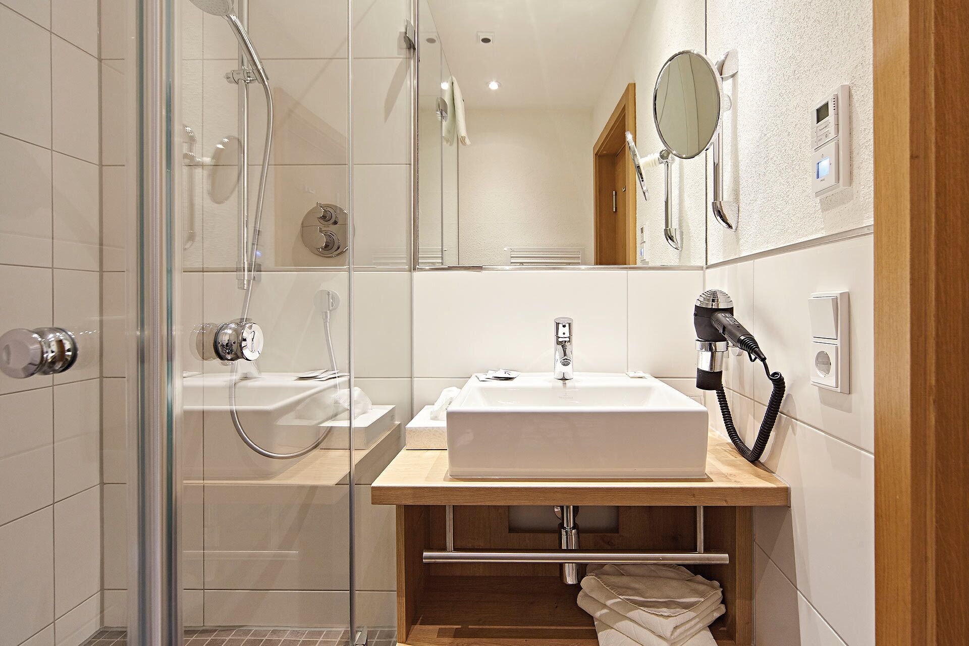 Une salle de bain moderne avec une douche à parois de verre, un lavabo blanc et un meuble-lavabo en bois.