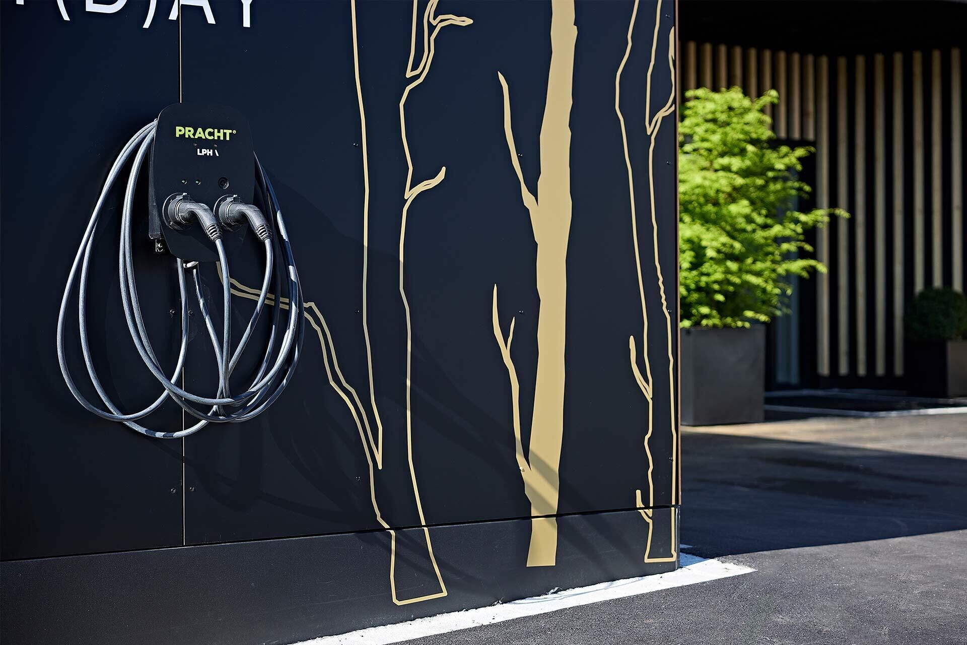 Un mur noir orné de motifs d’arbres dorés et une station de recharge « PRACT » LPH.