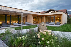A modern house with a wooden exterior, large glass windows, and a well-maintained garden with flowers and a rock centerpiece. - Hotel Restaurant Die Krone (Immenstadt im Allgaeu)