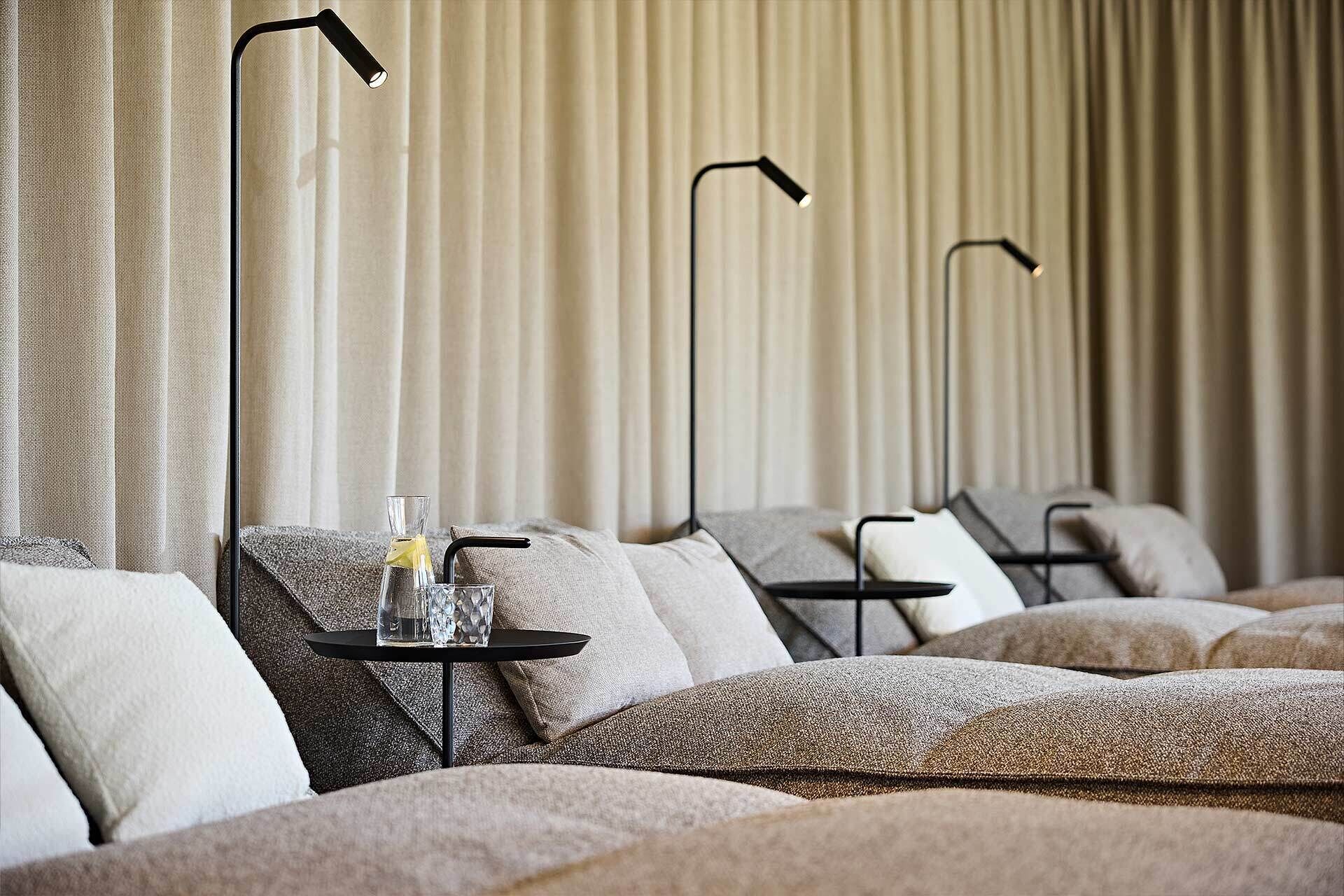 A hotel room with a bed, a small table with a glass and straw, and three black floor lamps.