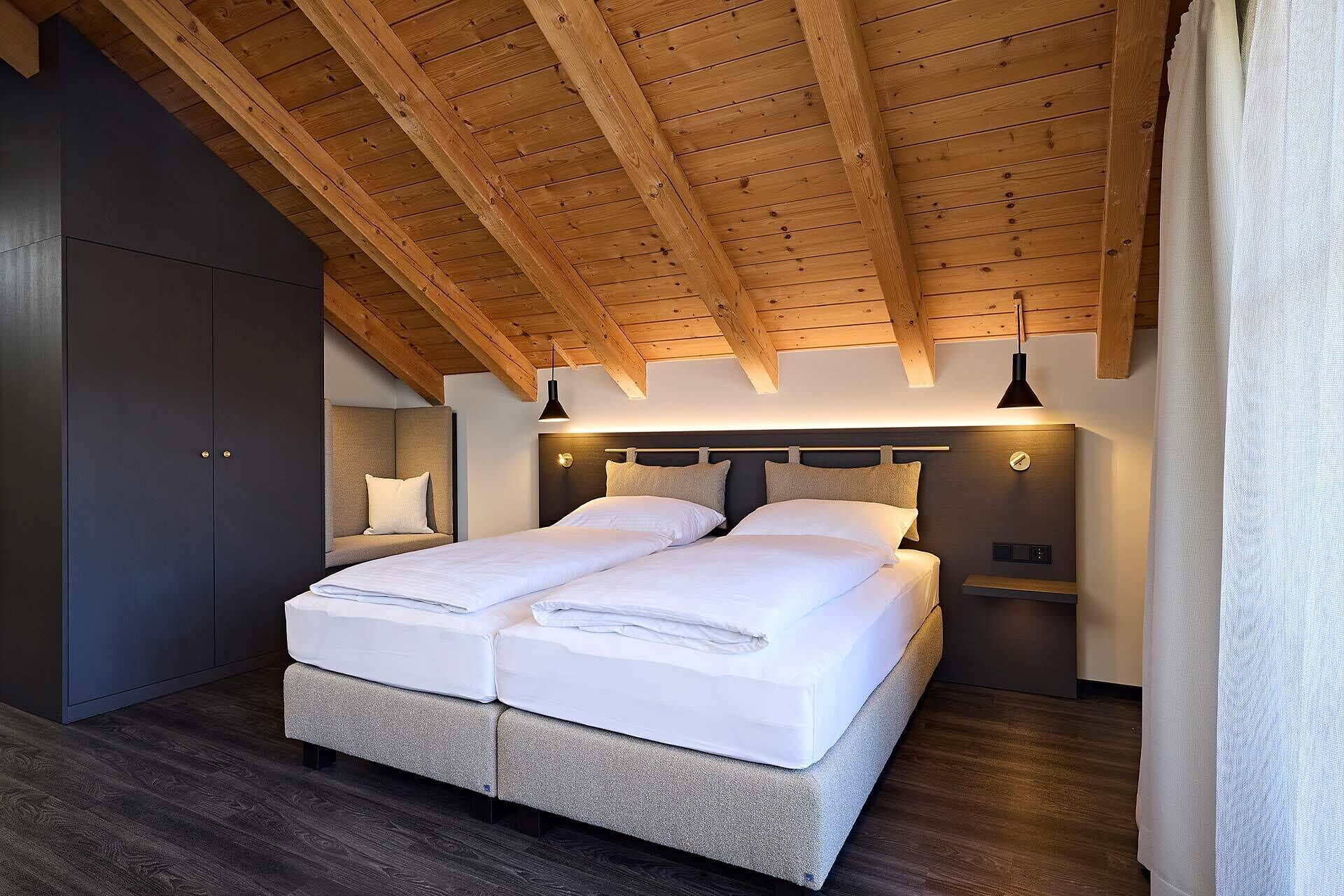 Une chambre avec un plafond en bois, un lit avec une literie blanche, une table de chevet et une armoire.