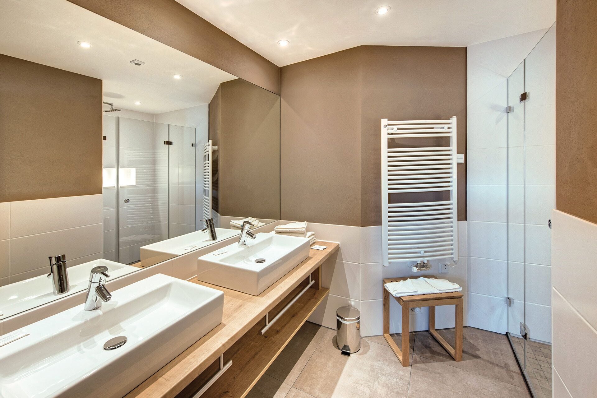A modern bathroom with two sinks, a mirror, a towel rack, and a shower area.